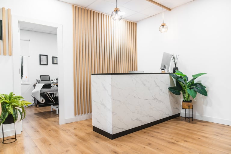 Clean physiotherapy clinic reception area featuring a marble counter, wood panel wall, and plants, leading to a treatment room